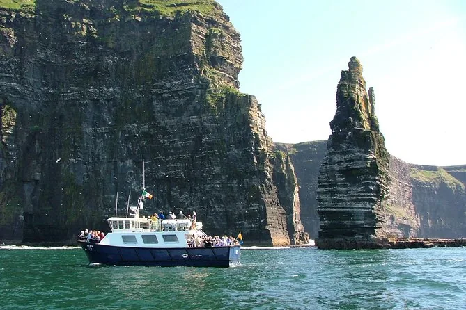Ein Ausflugsboot mit Passagieren an Deck unterhalb der Cliffs of Moher und eines hohen Brandungspfeilers
